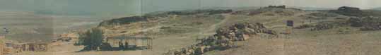 A panoramic view across the Masada Plateau. At left, near the flag, is the Snake Path gate. Panning right, you come across building nr. 12 (buildings of the Herodian Royal family) and right next to it, building nr. 11, a villa at the highest point of Masada. The large, partly roofed ruin to the extreme right is the Western Palace. At the right edge of the picture are the walls of the Byzantine church.